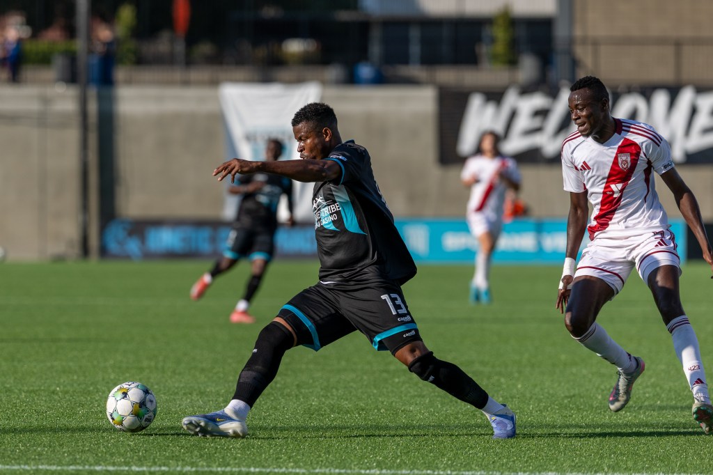 Lucky Opara steps to a soccer ball ahead of a defender in a white jersey