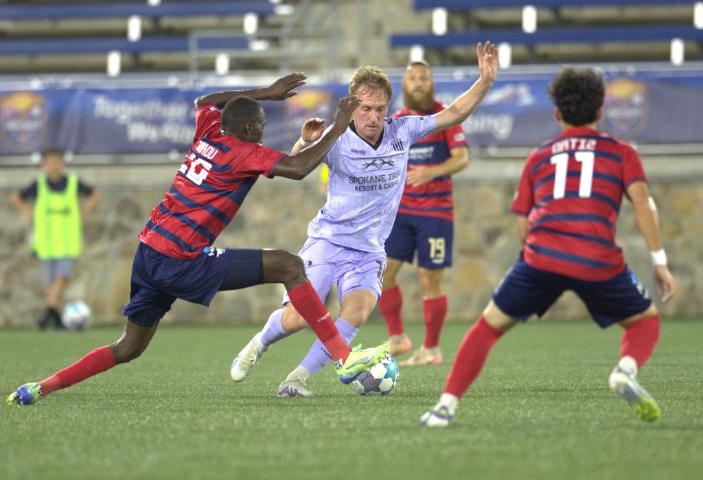 Derek Waldeck dribbles surrounded by defenders in red and blue striped jerseys