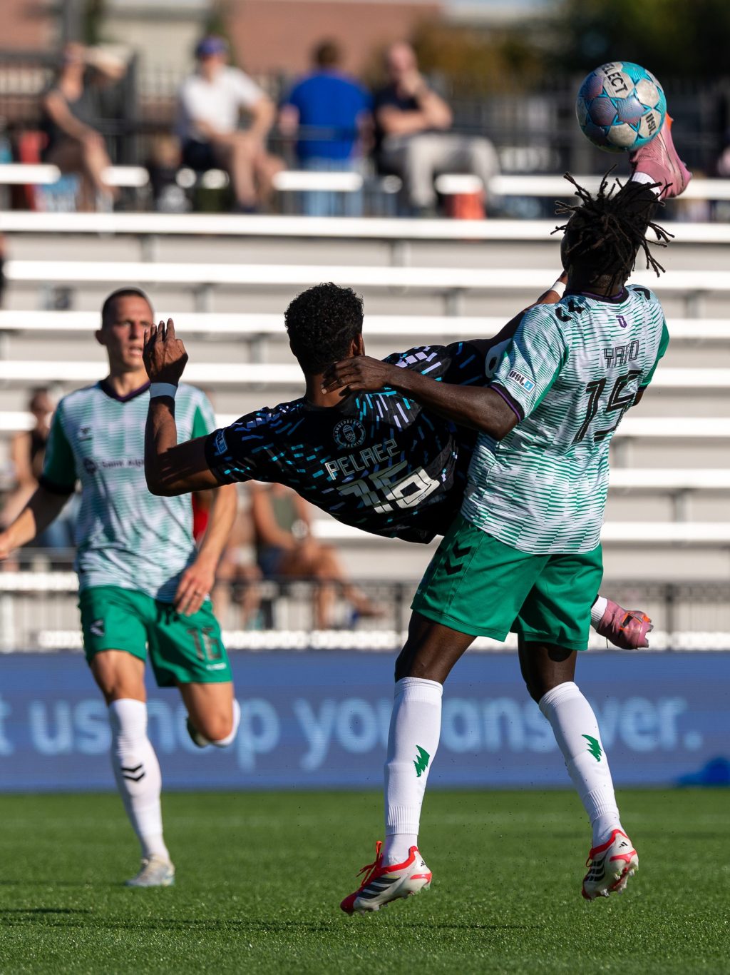 Anuar Pelaez attempts a bicycle kick between two defenders in green kits