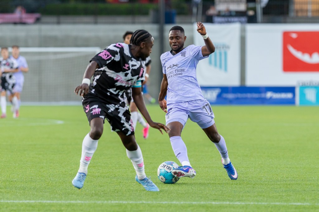 Andre Lewis, in a lilac soccer kit, dribbled toward the camera while a Forward Madison defender turns to challenge him