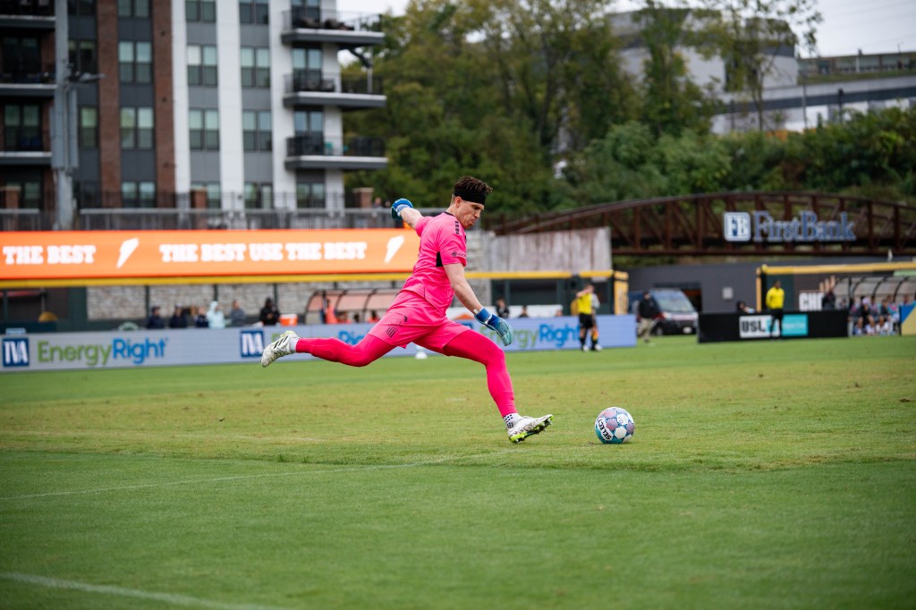 Sean Lewis steps to kick a ball, dressed in a pink goalkeeper kit
