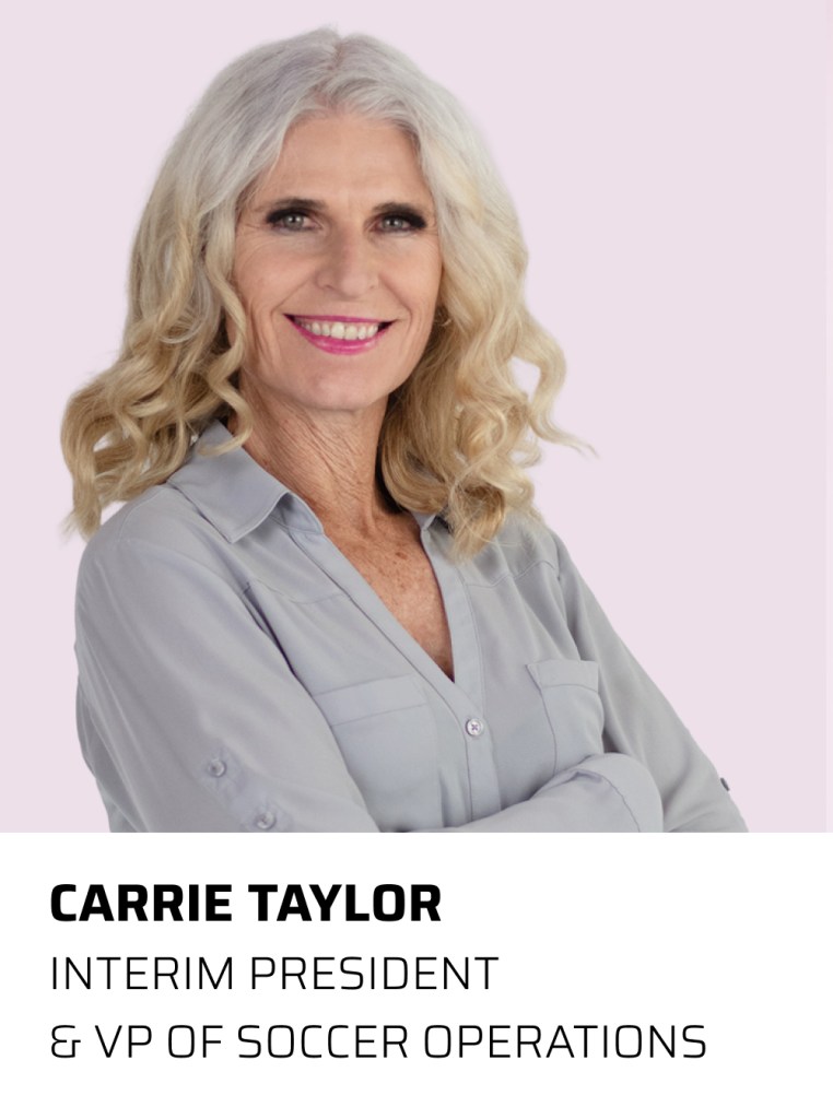 Portrait of Carrie Taylor, Interim President and VP of Soccer Operations, smiling and standing with arms crossed against a light pink background.